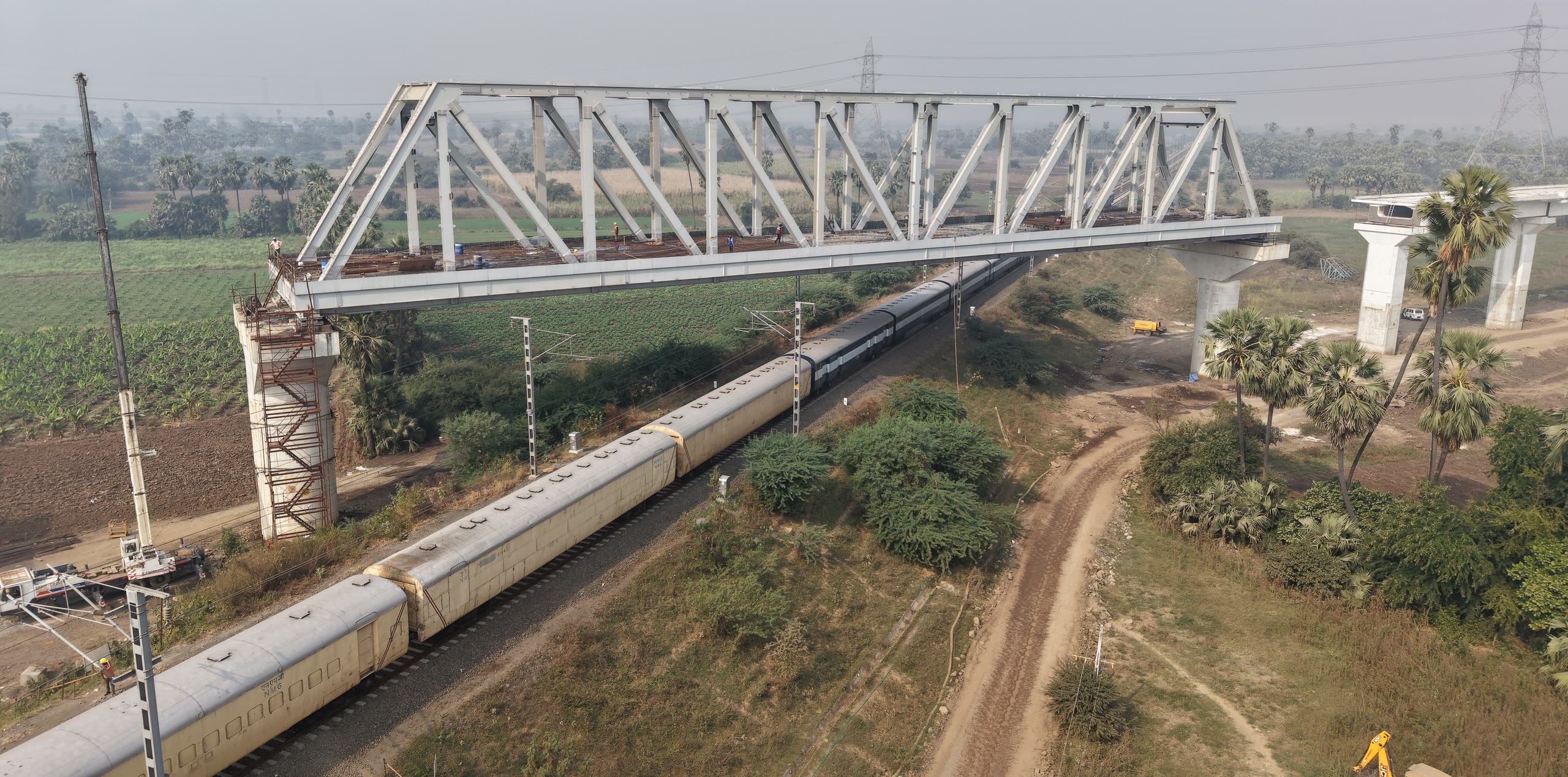 A train passes beneath a steel truss span launched for the high-speed rail corridor